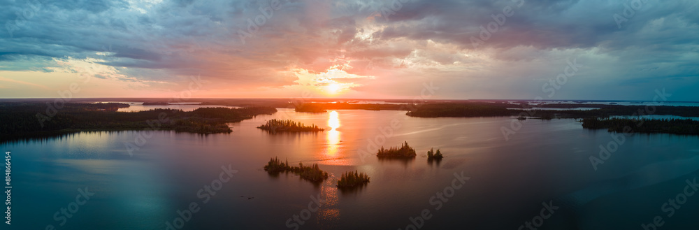 Aerial view of a large lake with small islands at sunset. The setting sun and colorful clouds are reflecting in the calm water.
Aerial view of a large lake with small islands at sunset. The setting sun and colorful clouds are reflecting in the calm water.