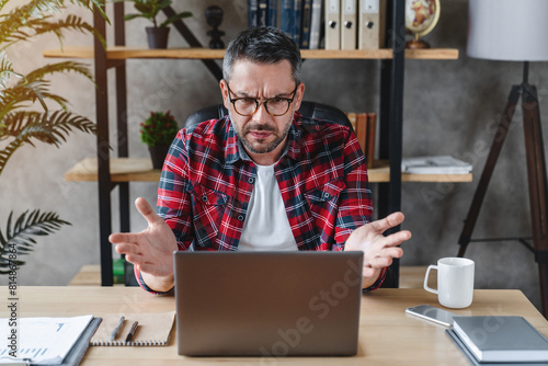 Unhappy caucasian man manager worker sitting a desk at home office look at laptop screen frustrated confused by gadget works wifi internet problem, error spam or scam on device. photo