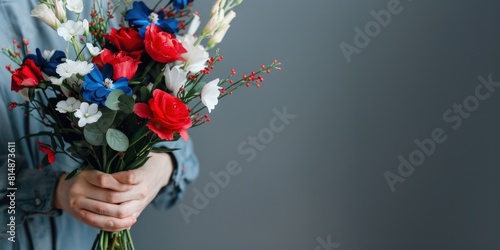 A person's hand holding a bouquet of flowers featuring red, white, and blue blossoms against a dark background, symbolizing a patriotic theme. 4th of July, american independence day © evgenia_lo