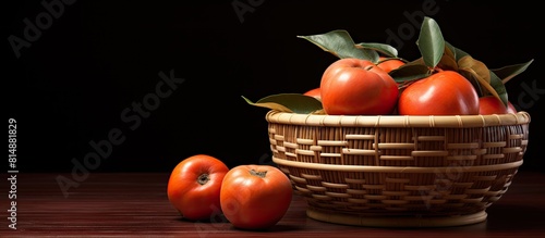 Close up copy space image of a Chinese lunar new year fruit design featuring a sliced sweet persimmon kaki in a bamboo sieve basket on a dark wooden table with a red brick wall background