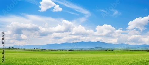 A picturesque countryside scene with mountains a clear blue sky and fluffy white clouds above a verdant farmland field Perfect for a copy space image on a sunny spring day