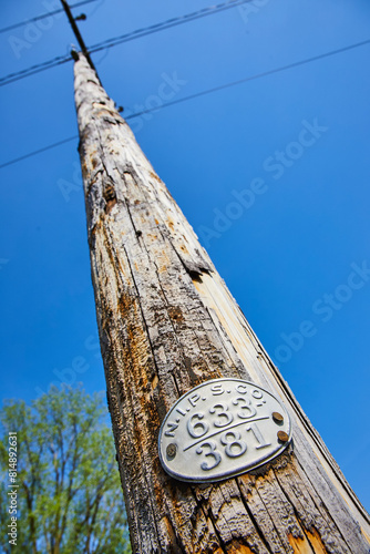 Weathered Utility Pole with Identifier Tag Against Blue Sky, Upward View photo