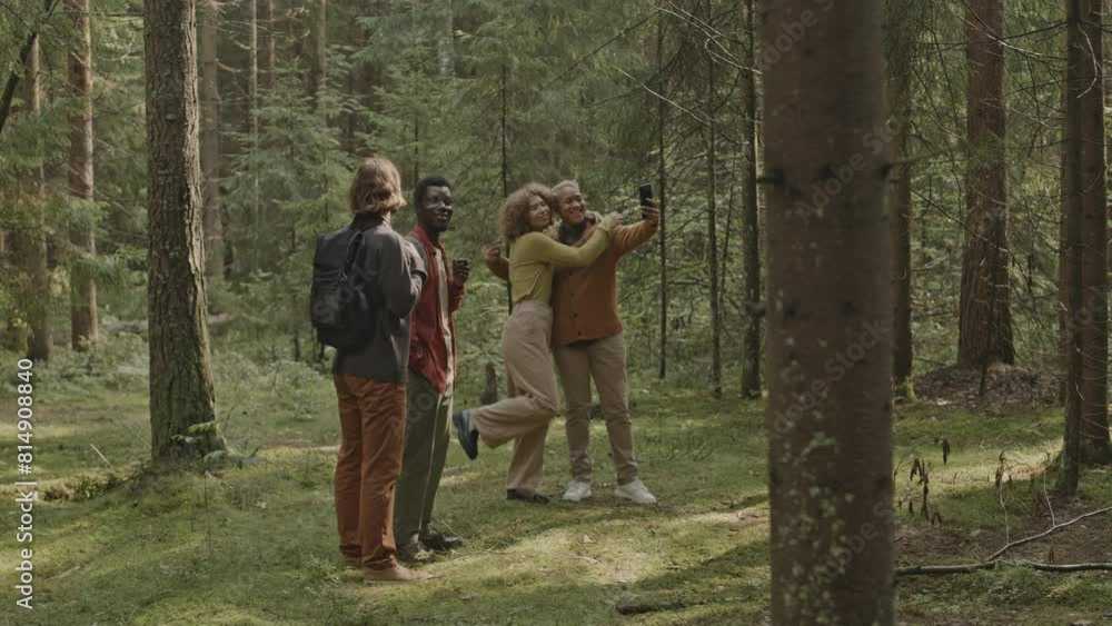 Company of friends taking break during hike in forest, couple taking selfie with phone and men discussing nature around Company of friends taking break during hike in forest, couple taking selfie with phone and men discussing nature around