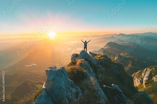 A person stands on a mountaintop at sunrise  arms raised in triumph