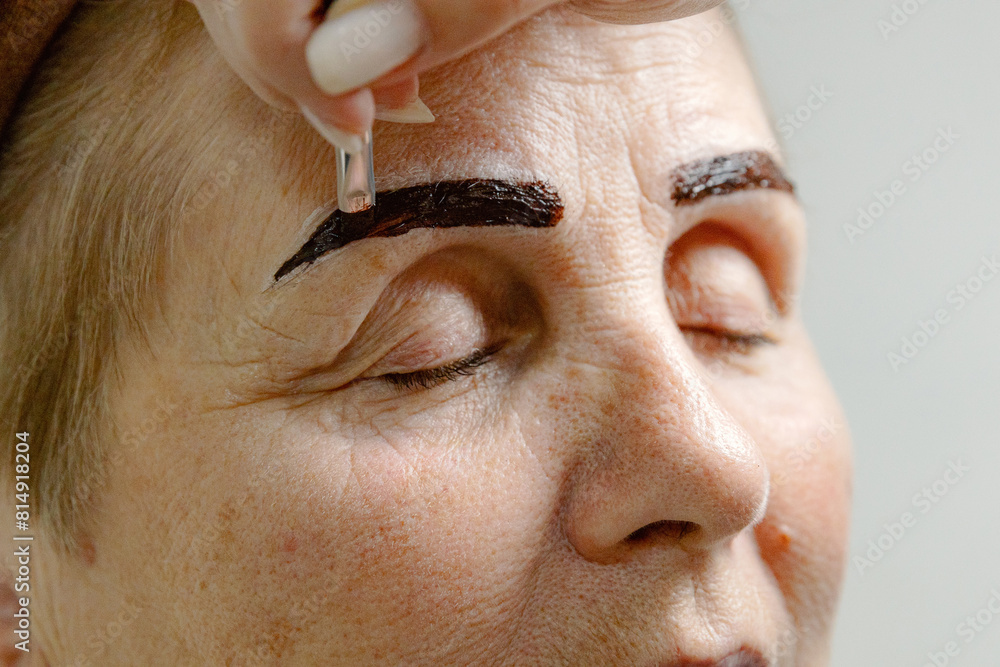 Fototapeta premium A cosmetologist paints the eyebrows of an elderly woman.