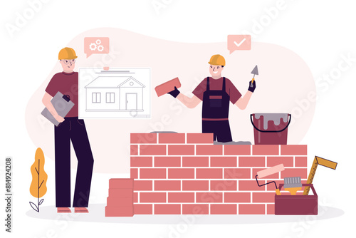 Engineer or architect shows blueprint of house for construction worker in uniform and helmet doing work. Builder puts brick wall.