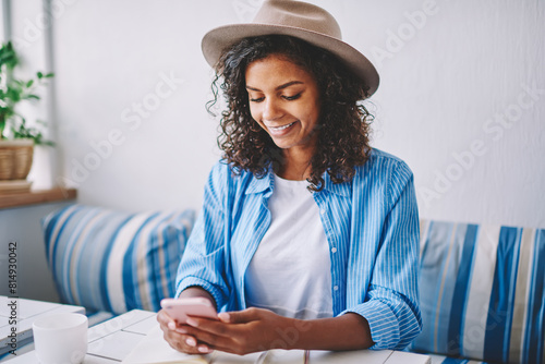 Smiling african female bogger installing application for creating new publication on content website, successful hipster girl in titfer checking updates for organiser on modern smartphone device