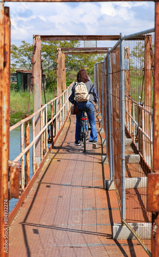 fearless young woman on a bicycle crosses a dangerous and rusty iron bridge © ChiccoDodiFC