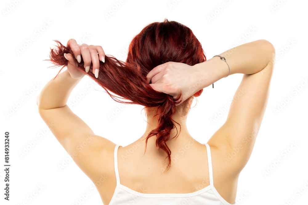 Rear of a young woman tying her long red wavy hair on a white background