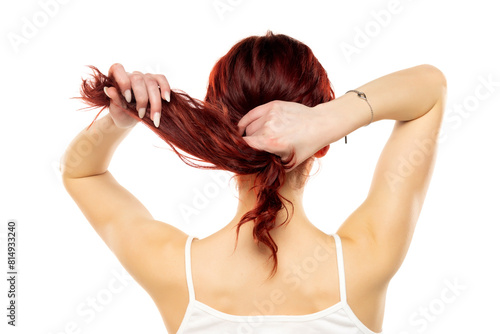 Rear of a young woman tying her long red wavy hair on a white background