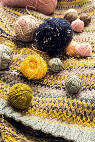 Multi-colored balls of knitting yarn on a hand-knitted jacquard background. Soft focus, shallow depth of field, blur, retro stylization.
