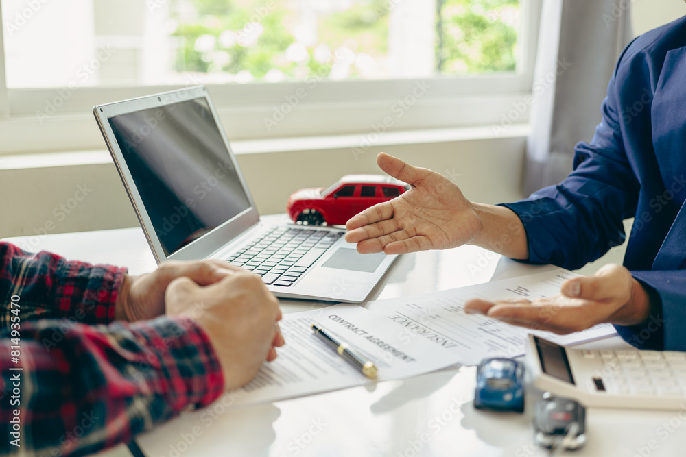 A close-up image of a salesperson introducing a customer sitting at a table with a small car and car keys. car dealer sales And the new owner has entered into a contract to sell and lease cars. A close-up image of a salesperson introducing a customer sitting at a table with a small car and car keys. car dealer sales And the new owner has entered into a contract to sell and lease cars.