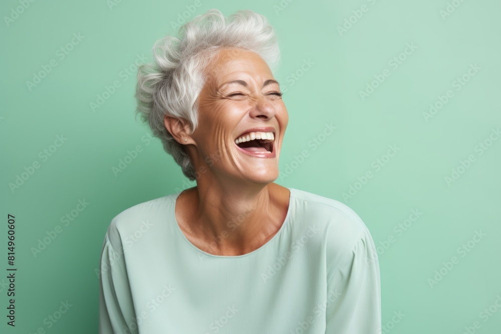 Portrait of a grinning woman in her 60s laughing isolated in pastel green background Portrait of a grinning woman in her 60s laughing isolated in pastel green background