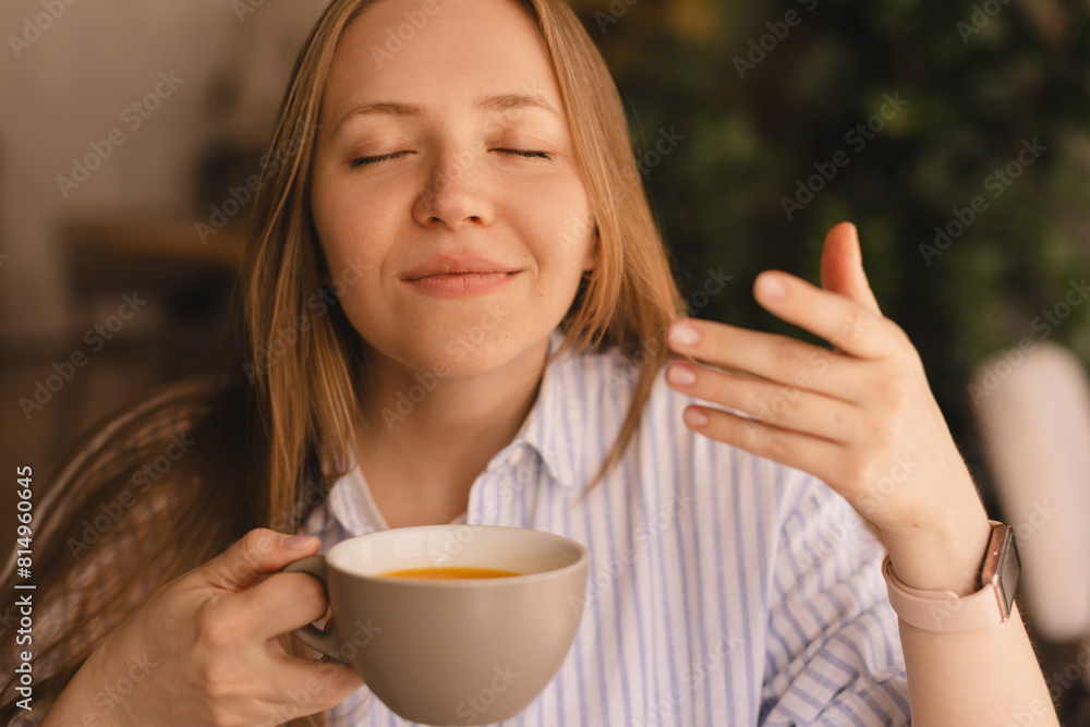 Portrait of gorgeous blonde smiling lady smelling, enjoying of coffee and drinking cappuccino from cup while resting in restaurant. Woman wear stripped shirt. Portrait of gorgeous blonde smiling lady smelling, enjoying of coffee and drinking cappuccino from cup while resting in restaurant. Woman wear stripped shirt.