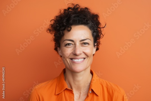 Portrait of a content woman in her 40s smiling at the camera while standing against pastel orange background