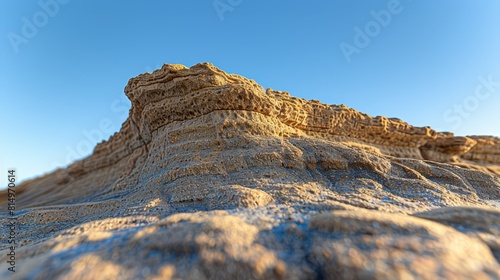  A tight shot of a rock formation against a backdrop of blue sky, with a scanty layer of sand in the foreground