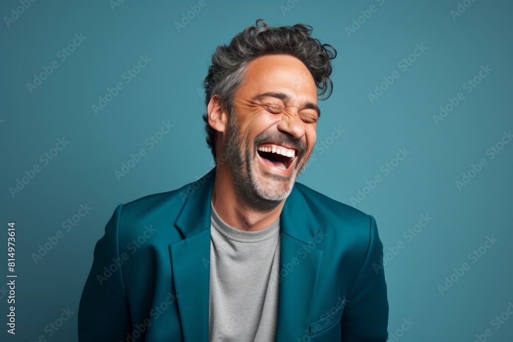 Portrait of a glad man in his 50s laughing while standing against pastel teal background