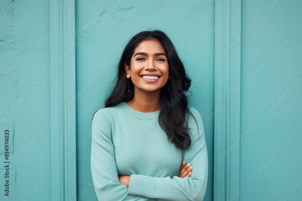 Portrait of a satisfied indian woman in her 20s with arms crossed isolated on pastel teal background Portrait of a satisfied indian woman in her 20s with arms crossed isolated on pastel teal background