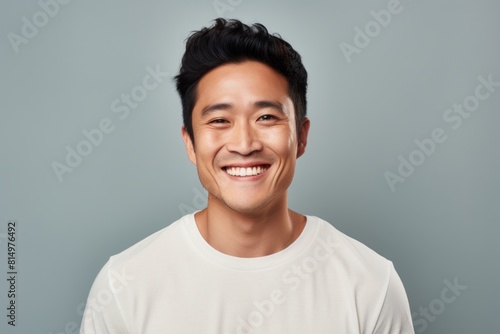 Portrait of a content asian man in his 30s smiling at the camera on pastel gray background