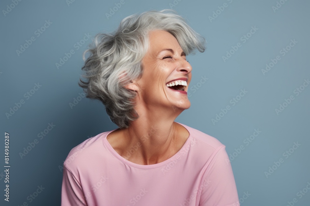 Portrait of a content woman in her 50s laughing on pastel gray background Portrait of a content woman in her 50s laughing on pastel gray background