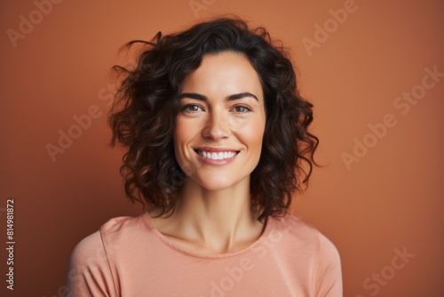 Portrait of a glad woman in her 30s smiling at the camera isolated in pastel brown background