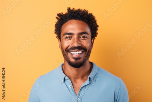 Portrait of a merry afro-american man in his 30s smiling at the camera while standing against pastel brown background