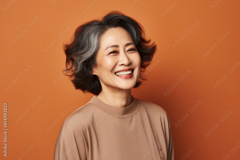 Portrait of a satisfied asian woman in her 50s smiling at the camera over pastel brown background Portrait of a satisfied asian woman in her 50s smiling at the camera over pastel brown background