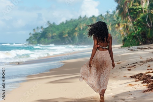 A woman in a maxi dress casually strolling on a sandy beach lined with palm trees, her hair tousled by the wind