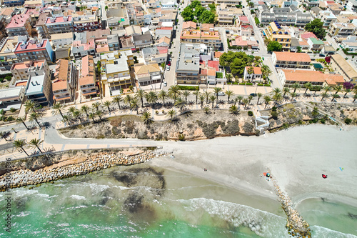 Aerial shot, drone point of view panoramic image of Torre de la Horadada townscape with sandy beach, turquoise bay and city rooftops at sunny summer day. Costa Blanca, Alicante, Spain