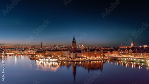Stockholm, Riddarholmen, the old town, at night in summer, green aurora borealis, nothern lights partly visible in the sky. Orange and yellow city lights, medieval buildings, churches and city skyline