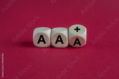 Turned a wooden cube and changes the expression AAA to AA plus. Beautiful red background. Symbol for a downgrade in a financial rating.