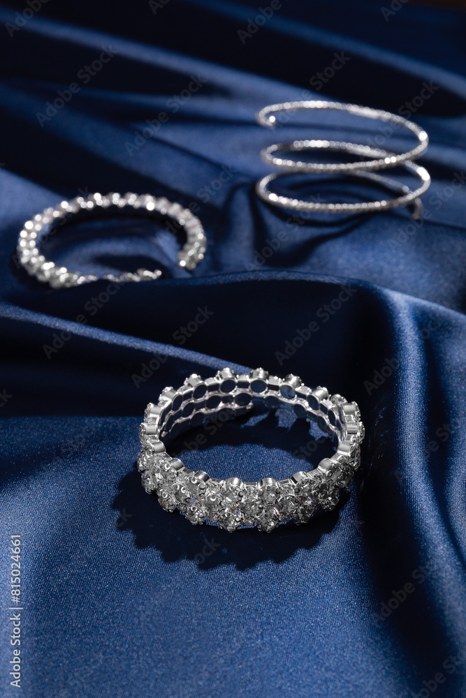 Fototapeta premium Bracelets with diamonds on a background of blue silk. Expensive jewelry. Natural gems. Top view. Space for text.