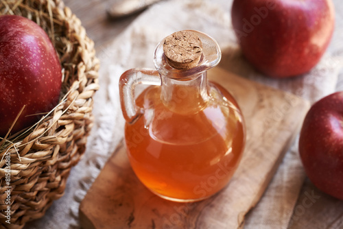 A bottle of apple cider vinegar with fresh apples on a table