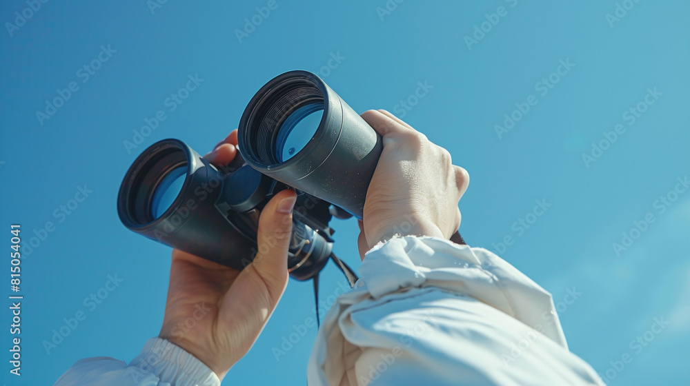 Obraz premium Person Holding Black Binoculars Against Clear Blue Sky Exploring Vast Horizons