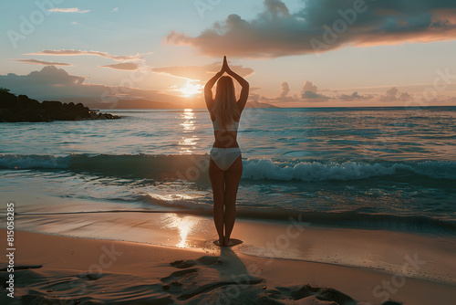 a woman practicing mindfulness and gratitude while doing yoga on a peaceful beach at sunset, promoting holistic well-being and positive mental health practices during the summer © kashiStock