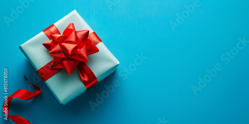 Blue background hosts a beautifully wrapped gift box Happy Birthday. Surprise gift wrap with red ribbon bow on a  Present box  decoration of gift on table  top view with copy space.