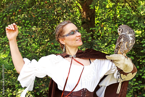 Eine Frau, als mittelalterliche Jägerin verkleidet, hat einen Waldkauz auf ihrer Hand