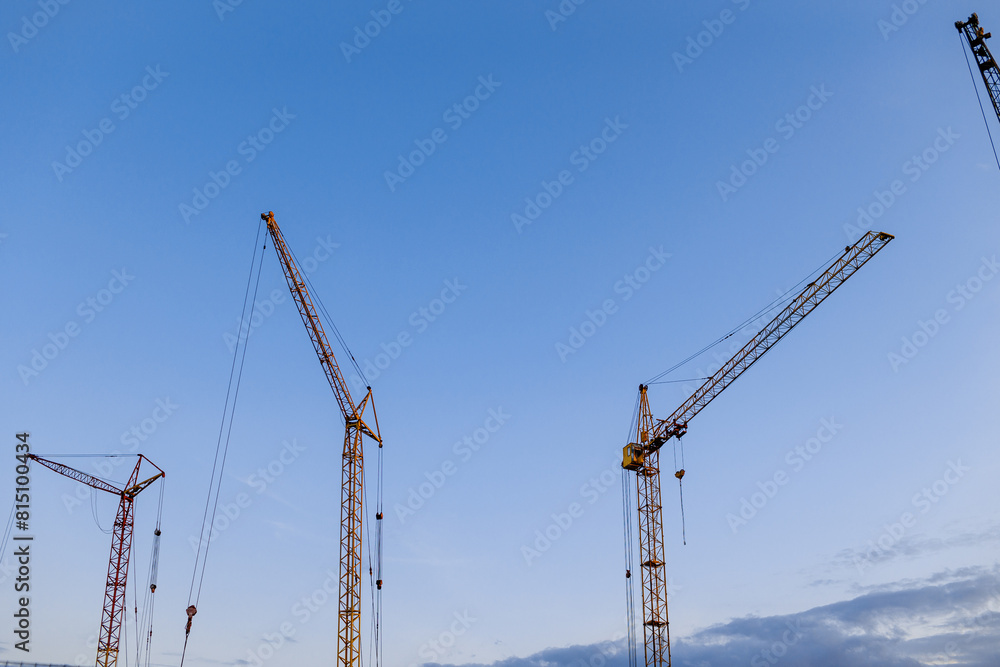 Construction site. Many tower cranes on dusk blue sky background. Construction multi-storey residential and commercial real estate. Industry new building business. Mortgage concept Construction site. Many tower cranes on dusk blue sky background. Construction multi-storey residential and commercial real estate. Industry new building business. Mortgage concept