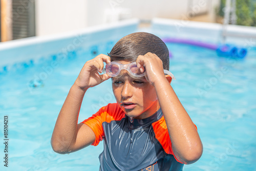 Boy in a pool with goggles hanging around his neck, a moment of rest during swim play. photo