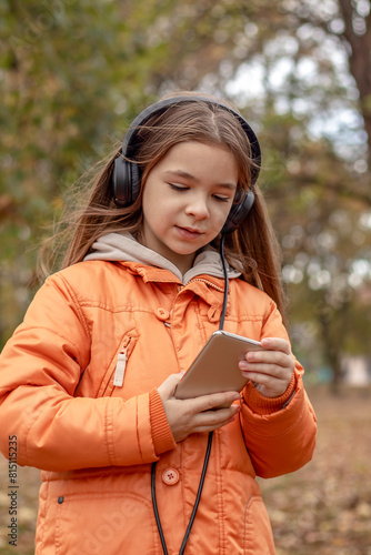 A cheerful girl listens to music on headphones in an autumn park.