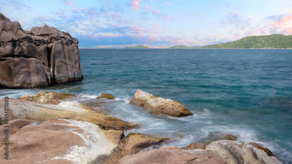 Naklejka premium A rocky shoreline with a calm ocean in the background. The water is a deep blue color and the sky is a light blue color