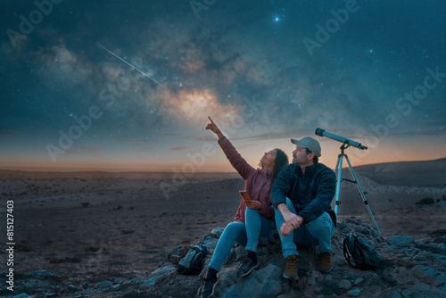 two people sitting in the desert watching the stars and Milky Way next to a telescope, stargazing and exploration concept 