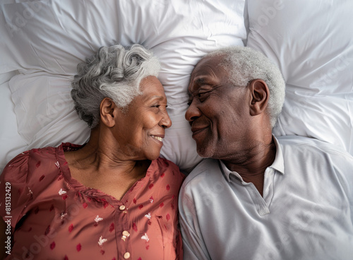 Elderly black couple lying in bed together, smiling at each other.