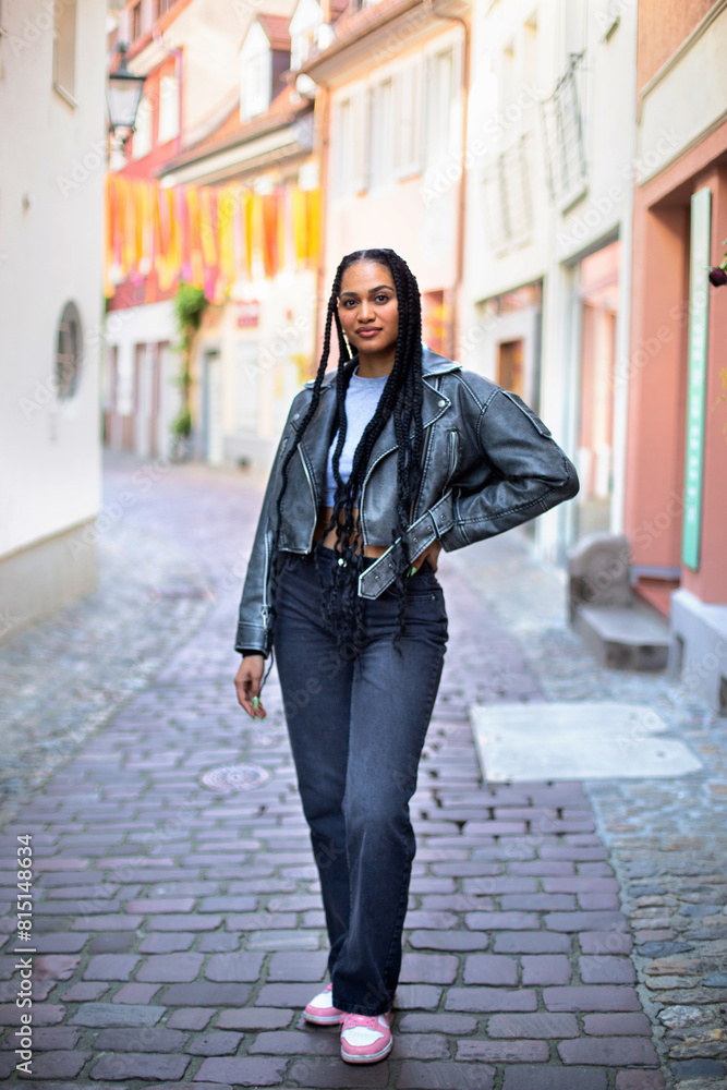 stylish young black female with afro braids a leather jacket is staying on the narrow street
