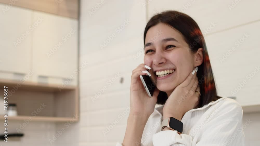 Young attractive woman in casual clothes standing in the cozy kitchen at home, talking with a friend on a smartphone and cheerfully laughing close up Young attractive woman in casual clothes standing in the cozy kitchen at home, talking with a friend on a smartphone and cheerfully laughing close up