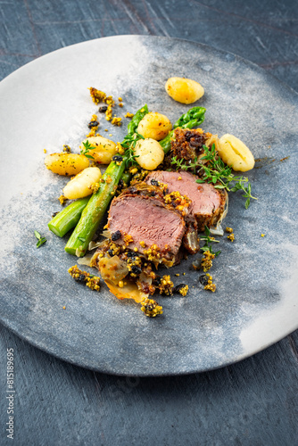 Fried mangalica pork tenderloin coated with crashed pistachio nuts, grated parmesan and chopped cranberries served with green asparagus and gnocchi as close-up on a Nordic design plate  © HLPhoto