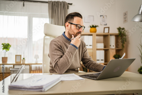 One adult man sit at office and look, read document on laptop at office