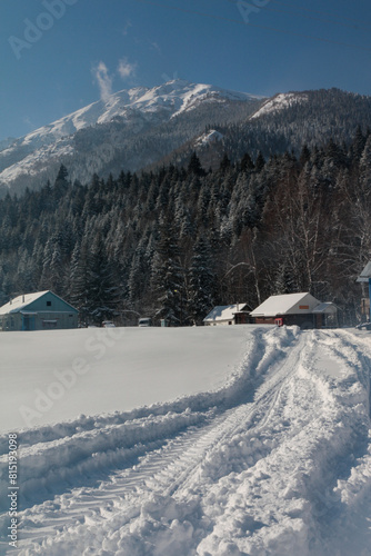 A snow-covered field with a blue building against the background of mountains. A village in a mountain valley in winter. Football goal without a net.