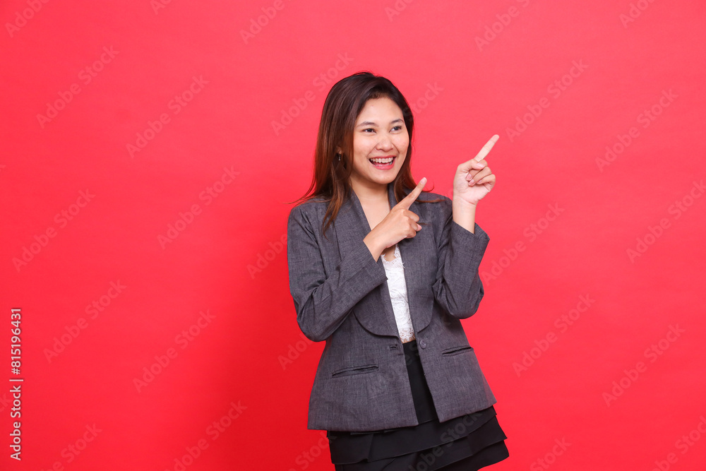 gesture of a cheerful Asian office girl, candid, hand pointing to the top left, wearing a gray jacket and black mini skirt on a red background. for corporate concepts, publications and advertising gesture of a cheerful Asian office girl, candid, hand pointing to the top left, wearing a gray jacket and black mini skirt on a red background. for corporate concepts, publications and advertising