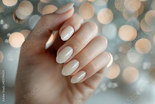 A beautiful woman s hand with perfect manicure on bokeh background  close up. The color of the nail polish is beige and white